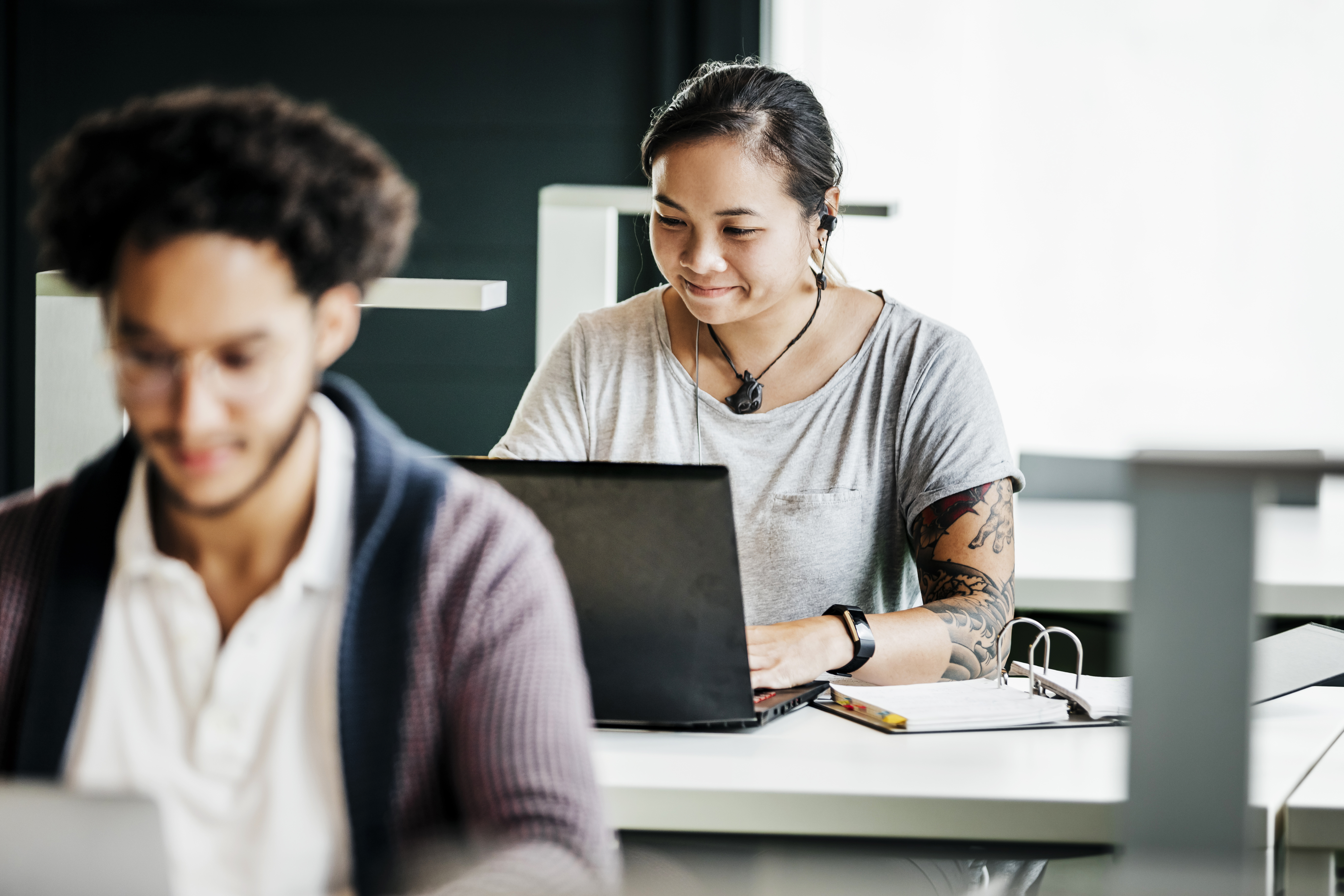 Zwei Studierende sitzen jeweils vor ihrem Laptop an Arbeitstischen.